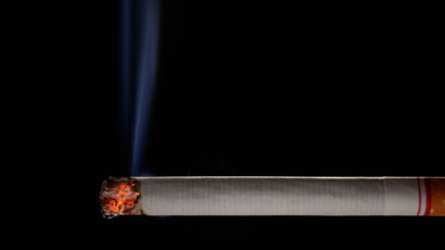 Lit and burning cigarette with smoke on black background
