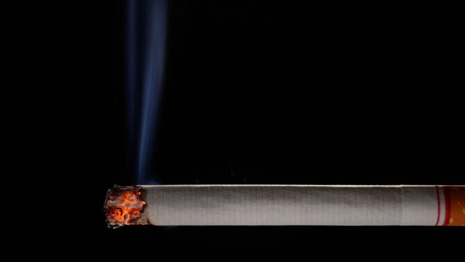 Lit and burning cigarette with smoke on black background