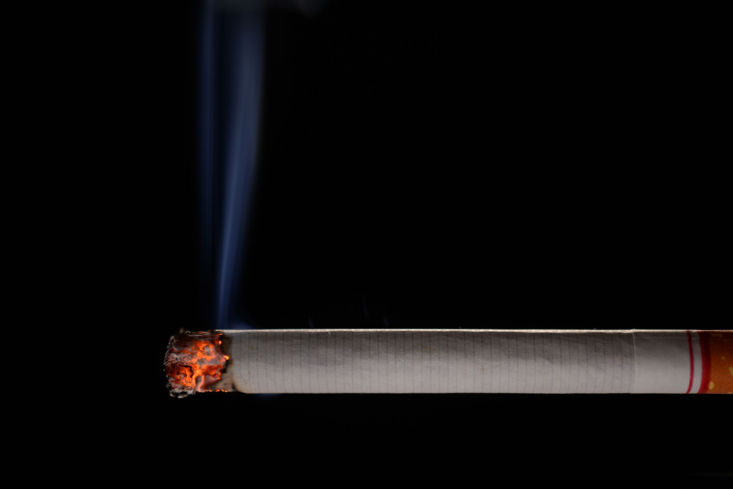 Lit and burning cigarette with smoke on black background